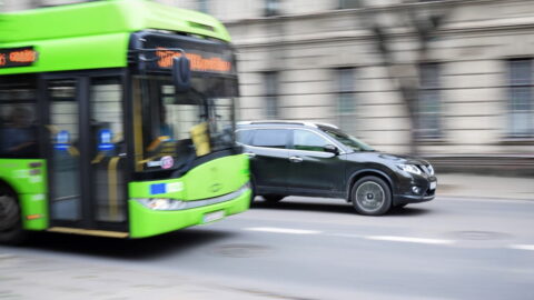 Green bus and a black car driving on a street